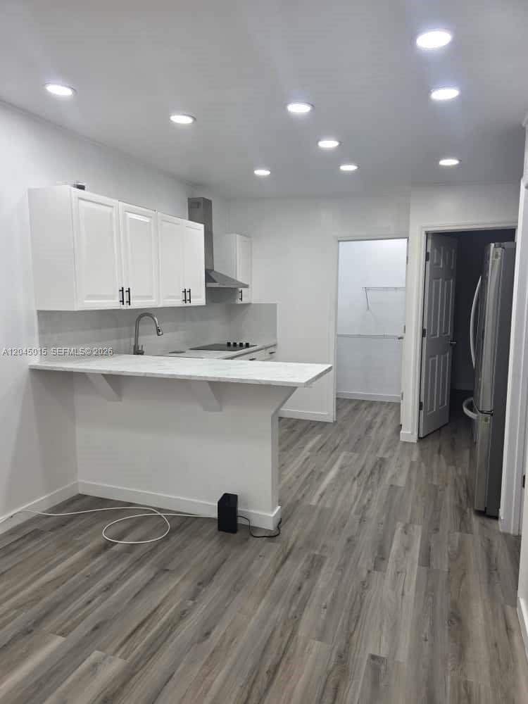 A modern kitchen features white cabinets, a breakfast bar, and light wood-look flooring — 23 Miami Gardens Rd # 3, West Park FL 33023, WEST PARK, FL