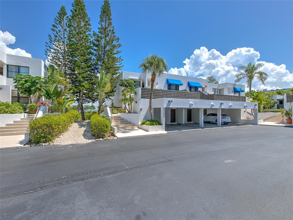 A white multi-story building features covered parking, blue awnings, and stairs leading to entrances — 817 BAYPORT WAY UNIT 817, LONGBOAT KEY, FL