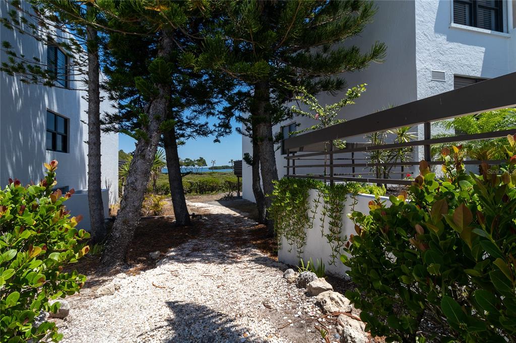 A gravel path leads between two white buildings toward a view of the ocean — 817 BAYPORT WAY UNIT 817, LONGBOAT KEY, FL