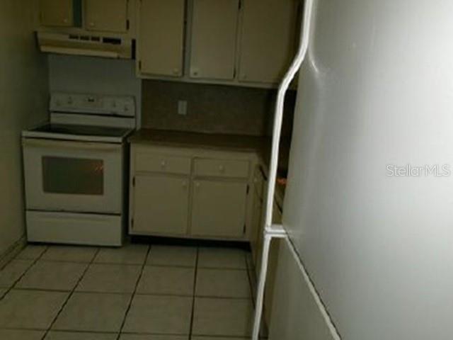 A kitchen features white cabinets, a white stove, and light-colored floor tiles — 6190 WOODLANDS BOULEVARD UNIT 309, TAMARAC, FL