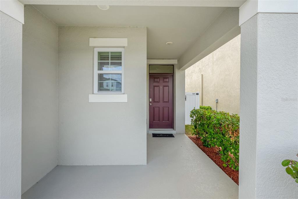 A covered entryway features a gray concrete floor, a window, and a dark purple front door — 3881 BRANT PLACE, LEESBURG, FL
