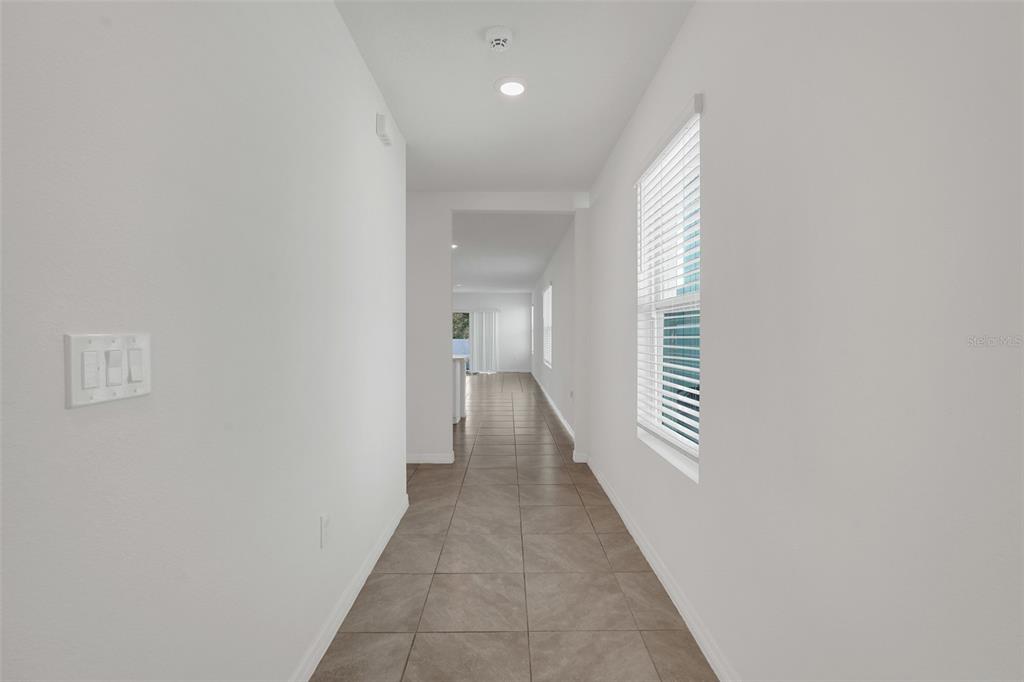 A long hallway with white walls and tiled flooring leads toward an open living area — 3881 BRANT PLACE, LEESBURG, FL