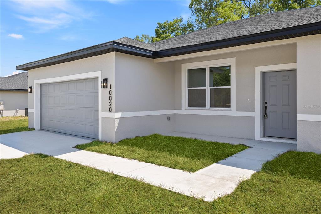 A single-story house exterior features a gray garage door, a front door, and a window — 44 W GULFSTREAM PLACE, CITRUS SPRINGS, FL