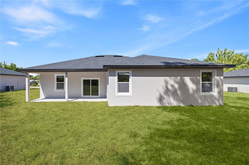The rear exterior of a single-story house features a covered patio and a grassy yard — 44 W GULFSTREAM PLACE, CITRUS SPRINGS, FL