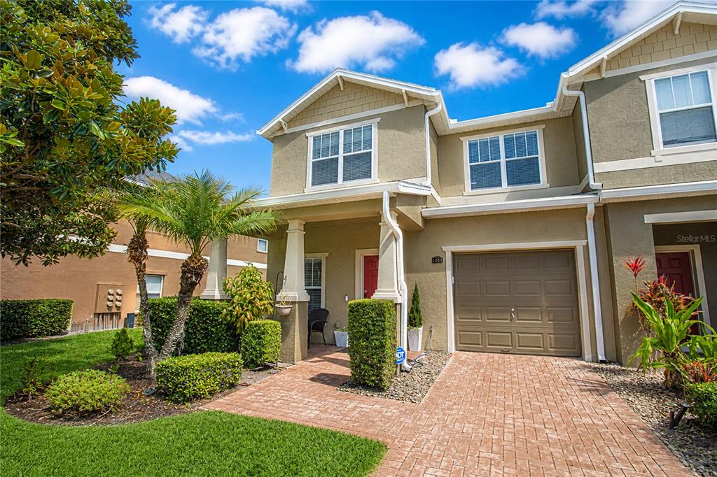 A two-story townhouse with a tan stucco exterior, a brick driveway, and a single-car garage — 1355 HONEY BLOSSOM DRIVE, ORLANDO, FL