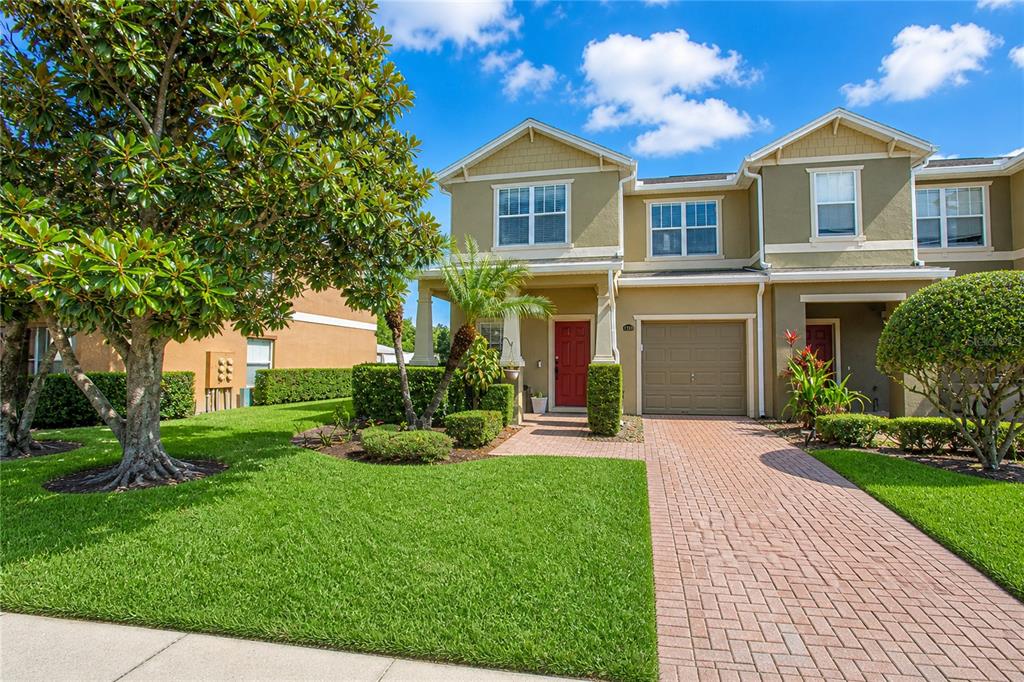 A two-story townhouse with a red front door, tan siding, and a brick paver driveway — 1355 HONEY BLOSSOM DRIVE, ORLANDO, FL