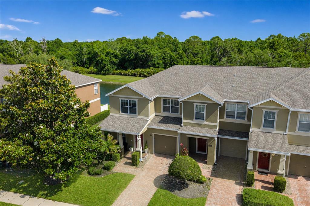 An aerial view of a multi-unit townhouse complex with a pond and wooded background — 1355 HONEY BLOSSOM DRIVE, ORLANDO, FL