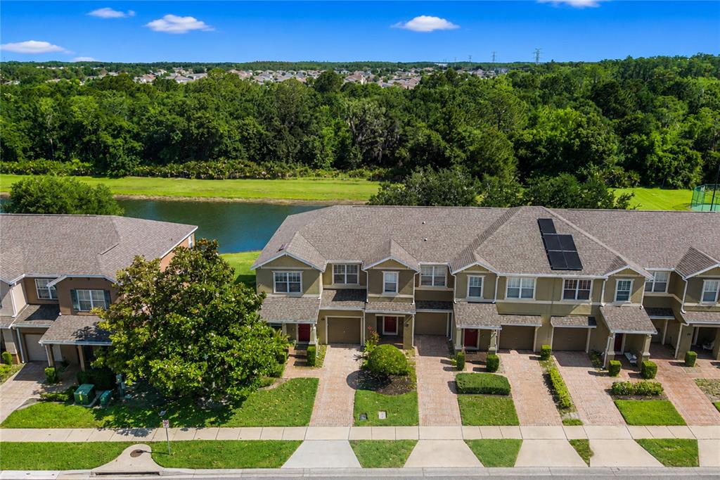 An aerial view shows a row of townhomes with brick driveways facing a small lake — 1355 HONEY BLOSSOM DRIVE, ORLANDO, FL