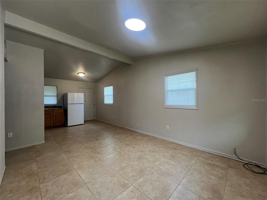 A kitchen and living area with beige tile flooring, light walls, and a white refrigerator — 13711 NW 158TH PLACE, ALACHUA, FL