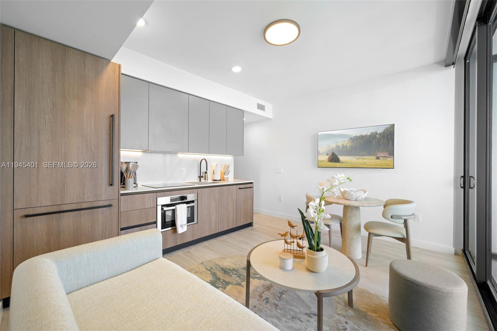 A modern studio apartment features a kitchenette with wood cabinets, a dining area, and seating — 580 72nd St # 1603, Miami Beach FL 33141, MIAMI BEACH, FL
