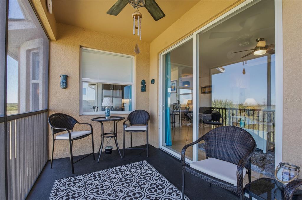 A covered patio features wicker chairs, a small table, a patterned rug, and sliding glass doors — 8105 GRAND ESTUARY TRAIL UNIT 402, BRADENTON, FL