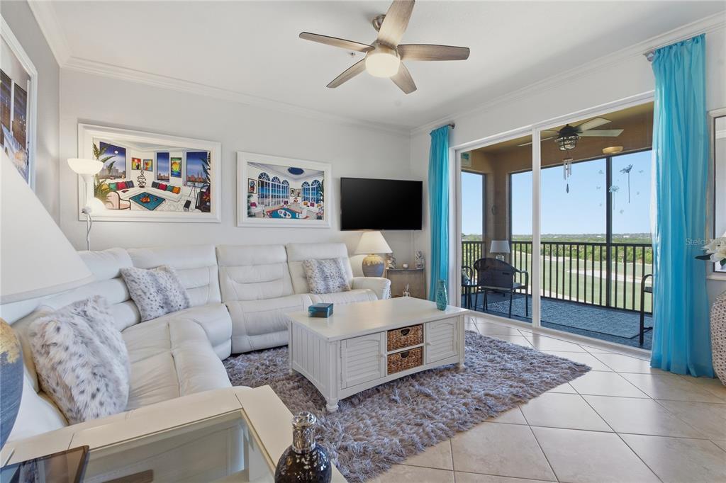 A living room features a white sectional sofa, a coffee table, and a balcony view — 8105 GRAND ESTUARY TRAIL UNIT 402, BRADENTON, FL