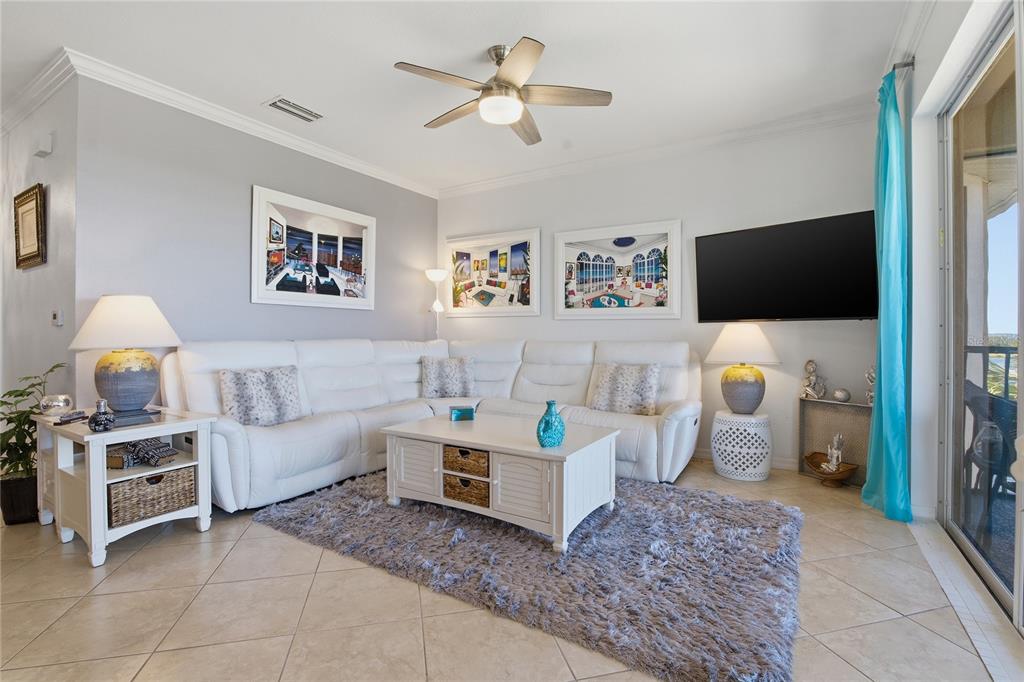 A living room with a white sectional sofa, coffee table, and a wall-mounted television — 8105 GRAND ESTUARY TRAIL UNIT 402, BRADENTON, FL