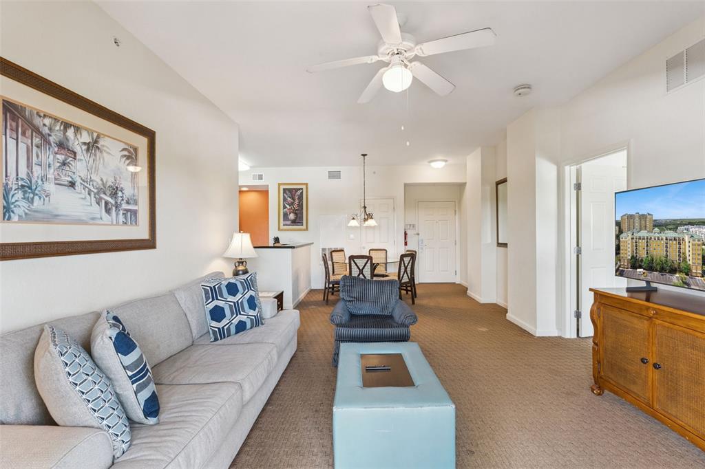 A living room with a sofa, armchair, ottoman, and dining area on carpeted flooring — 8100 POINCIANA BOULEVARD UNIT 2609, ORLANDO, FL