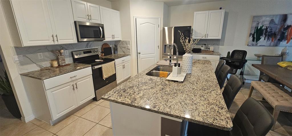 A kitchen features white cabinets, granite countertops, a center island, and stainless steel appliances — 1575 BARBERRY DRIVE, KISSIMMEE, FL