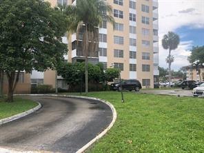 A paved driveway curves toward a multi-story apartment building surrounded by green lawns and trees — 4174 Inverrary Drive # 907, Lauderhill FL 33319, LAUDERHILL, FL