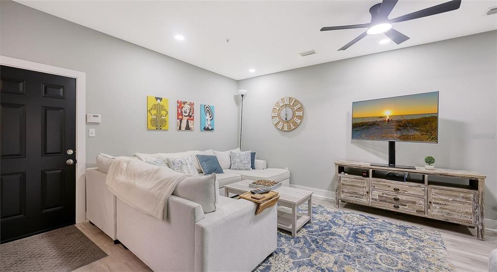 A living room features a sectional sofa, a television on a wooden console, and wall art — 3827 PARKRIDGE CIRCLE UNIT 1-102, SARASOTA, FL