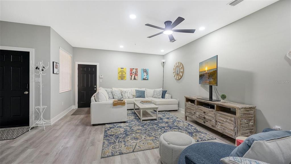A living room features a white sectional sofa, a wooden media console, and a blue rug — 3827 PARKRIDGE CIRCLE UNIT 1-102, SARASOTA, FL