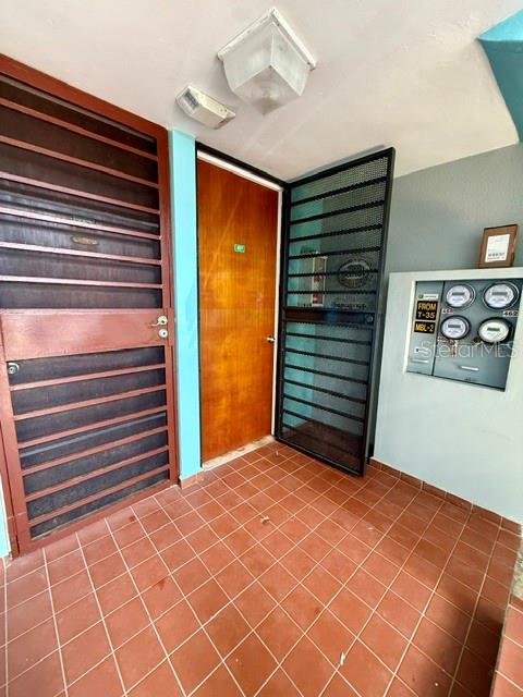 A tiled entryway features a wooden door, a metal security gate, and wall-mounted utility meters — 457 CHALETS DE LA PLAYA UNIT 457, VEGA BAJA, PR