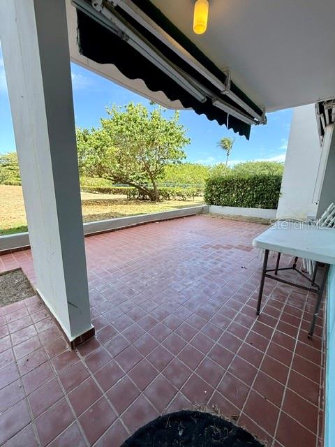 A tiled patio features a retractable awning and a view of trees and greenery — 457 CHALETS DE LA PLAYA UNIT 457, VEGA BAJA, PR