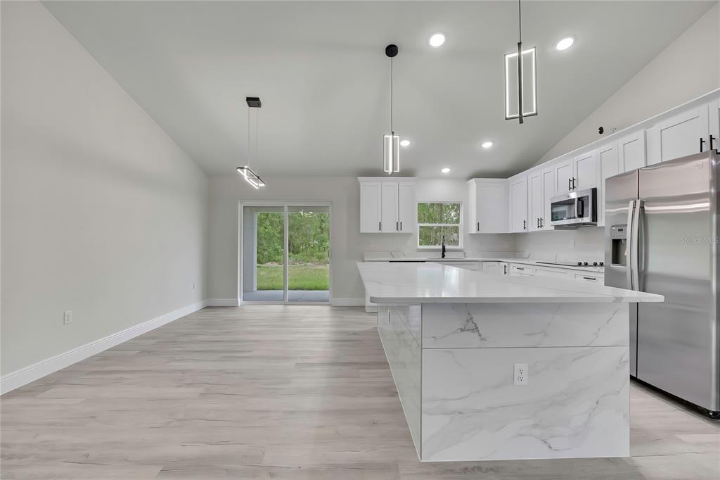 A modern kitchen features white cabinets, a marble-patterned island, and light wood-look flooring — 3261 W VIKING LANE, CITRUS SPRINGS, FL