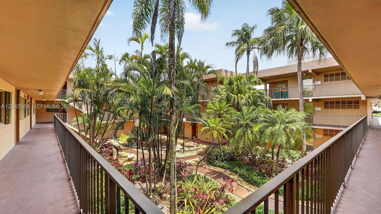 An outdoor walkway overlooks a landscaped courtyard with palm trees and tropical plants — 10975 SW 107th ST. # 202, Kendall FL 33176, KENDALL, FL