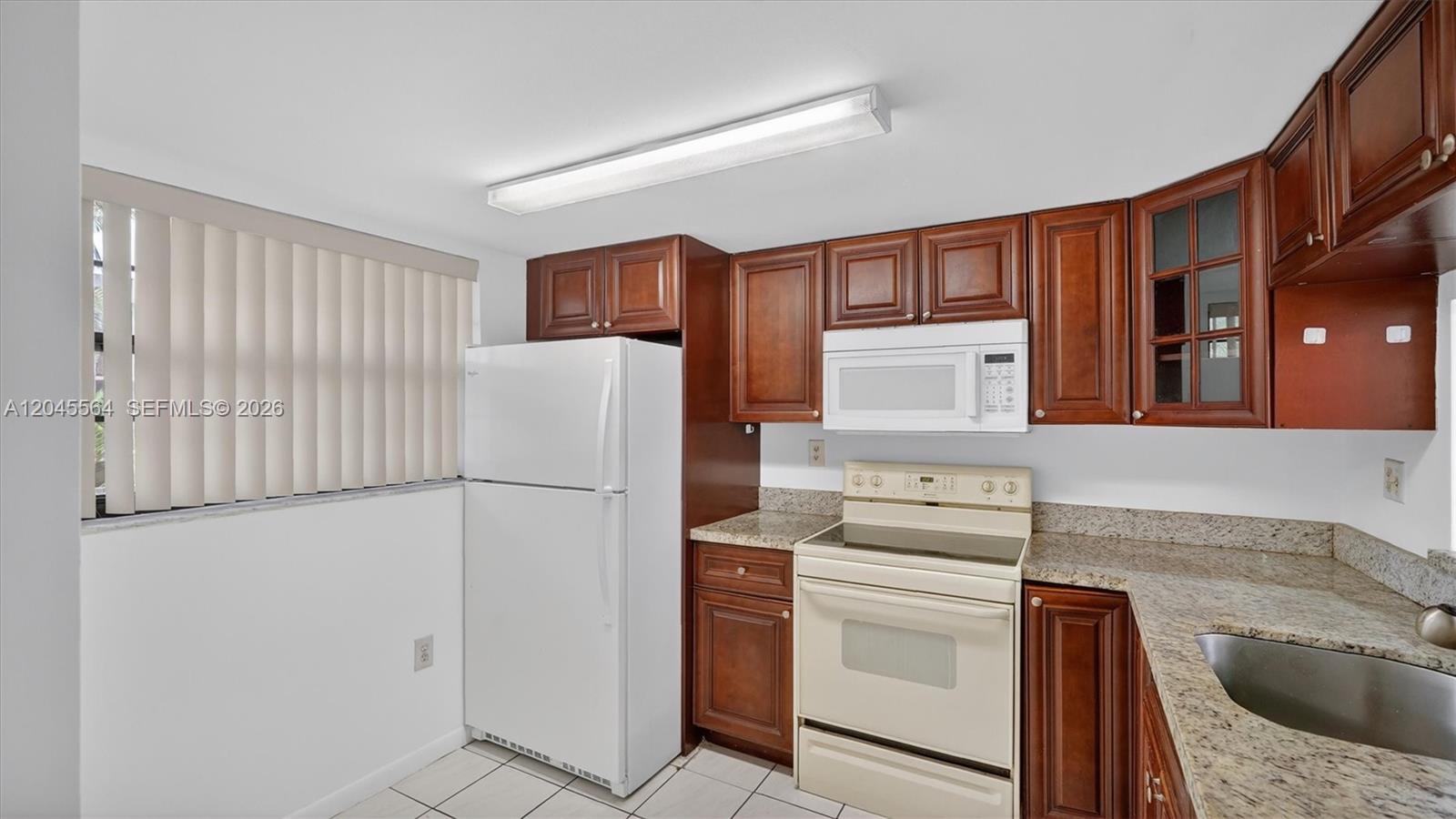 A kitchen features white appliances, dark wood cabinetry, and granite countertops — 10975 SW 107th ST. # 202, Kendall FL 33176, KENDALL, FL