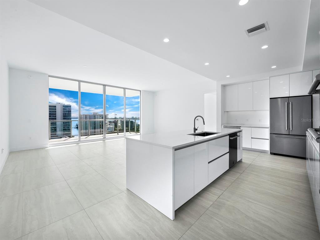 A modern kitchen with a white island and stainless steel refrigerator overlooks a balcony view — 301 QUAY COMMONS UNIT 1409, SARASOTA, FL