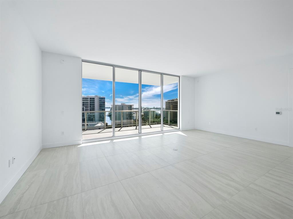 An empty room with light-colored tile flooring and floor-to-ceiling windows overlooking a waterfront cityscape — 301 QUAY COMMONS UNIT 1409, SARASOTA, FL