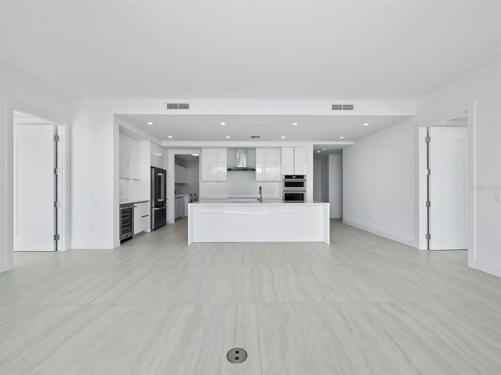 A modern, minimalist kitchen features white cabinetry, a central island, and light-colored tile flooring — 301 QUAY COMMONS UNIT 1409, SARASOTA, FL