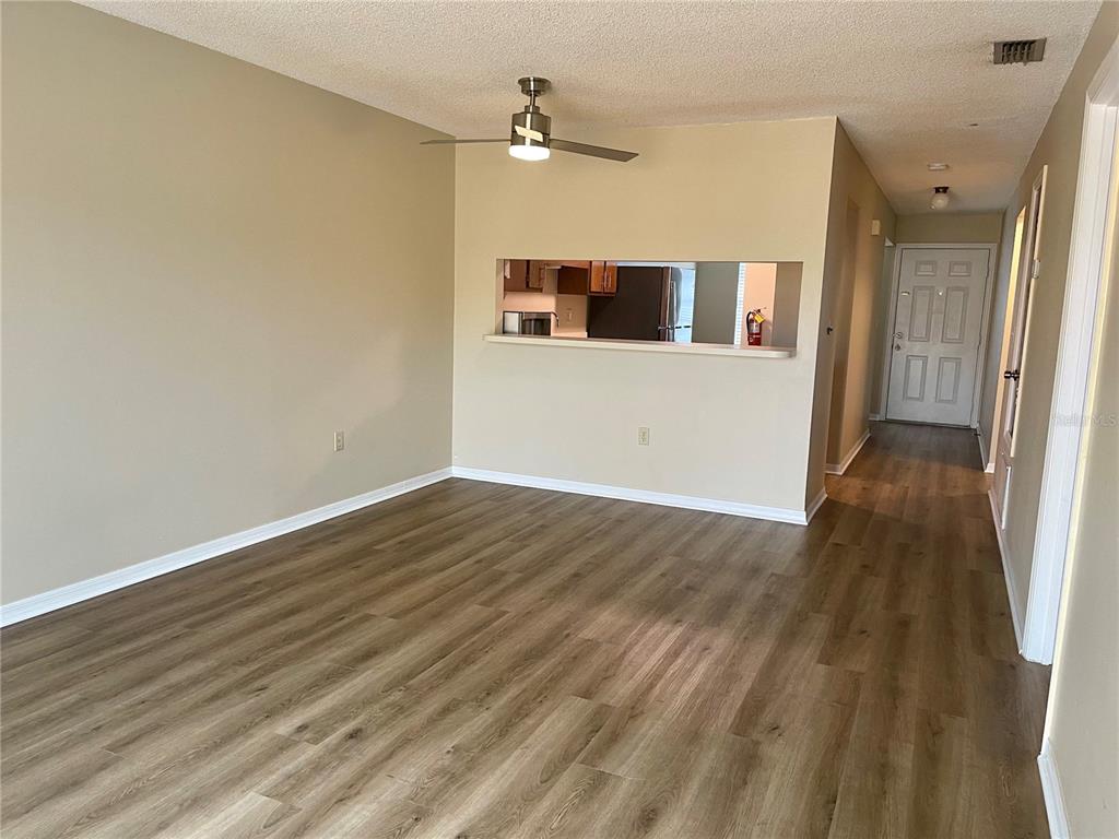 An empty living room features light-colored walls, wood-look flooring, a ceiling fan, and a pass-through window — 2341 ARUBA COURT, KISSIMMEE, FL
