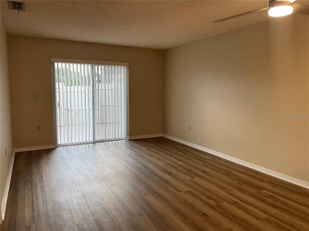 An empty room features wood-look flooring, beige walls, and a sliding glass door with blinds — 2341 ARUBA COURT, KISSIMMEE, FL