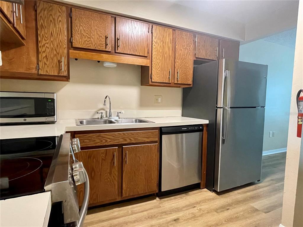 A kitchen features wood cabinets, stainless steel appliances, a double sink, and wood-look flooring — 2341 ARUBA COURT, KISSIMMEE, FL