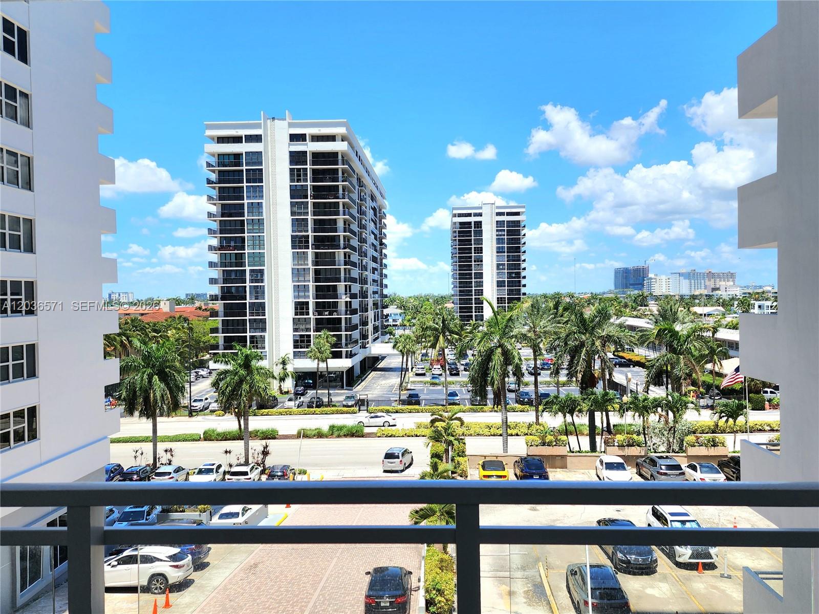 A balcony view overlooks a parking lot, palm trees, and two tall residential buildings — 2030 S Ocean Dr # 401, Hallandale Beach FL 33009, HALLANDALE BEACH, FL