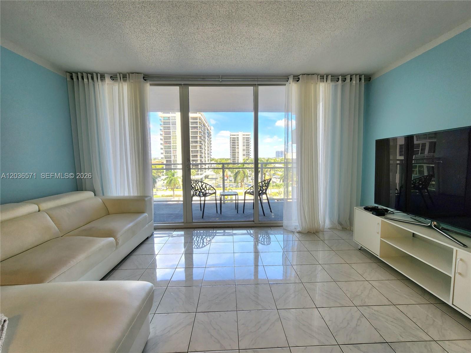 A living room features light blue walls, white tile flooring, a sofa, and a balcony view — 2030 S Ocean Dr # 401, Hallandale Beach FL 33009, HALLANDALE BEACH, FL
