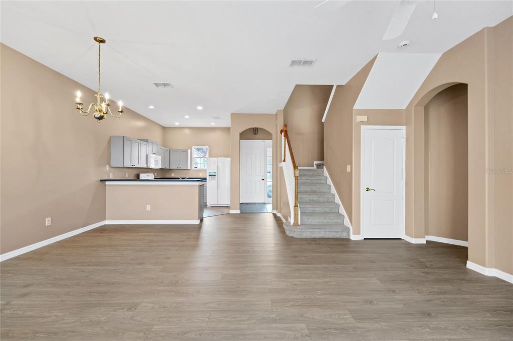 An open-concept living area features wood-look flooring, a kitchen with gray cabinets, and carpeted stairs — 516 BRUNELLO DRIVE, DAVENPORT, FL