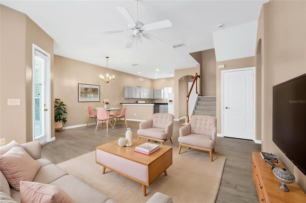 An open-concept living and dining area features light-colored furniture, wood-look flooring, and a staircase — 516 BRUNELLO DRIVE, DAVENPORT, FL