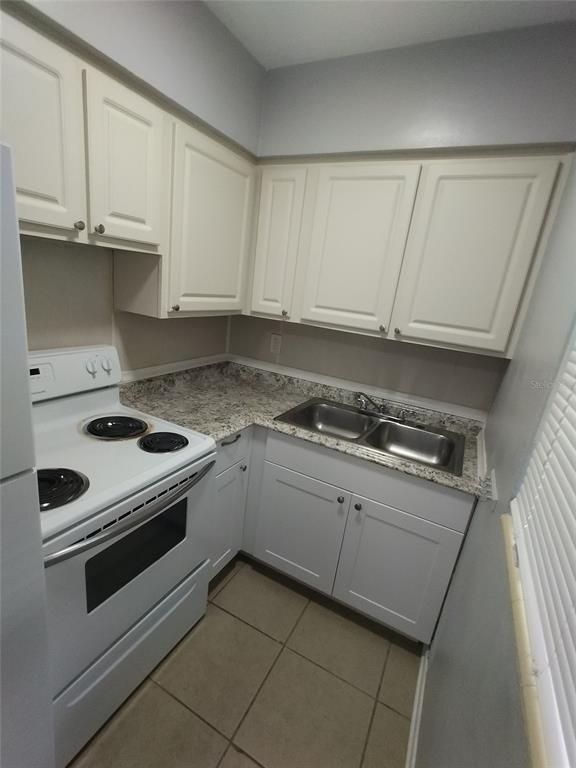 A small kitchen features white cabinets, a white electric stove, and granite-look countertops — 419 PINEAPPLE STREET UNIT 1, TARPON SPRINGS, FL