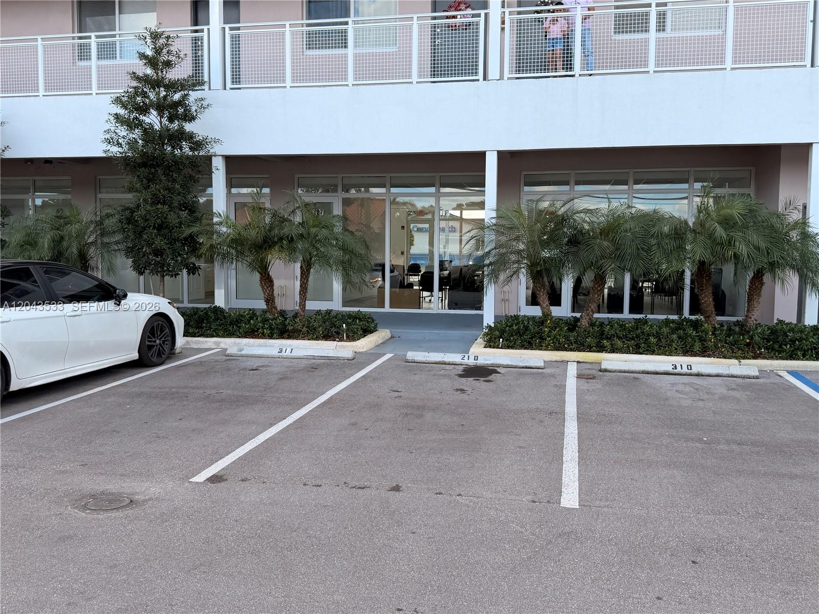 A white building exterior features ground-level office spaces with glass doors and parking spots — 665 E 49 ST, Hialeah FL 33013, HIALEAH, FL