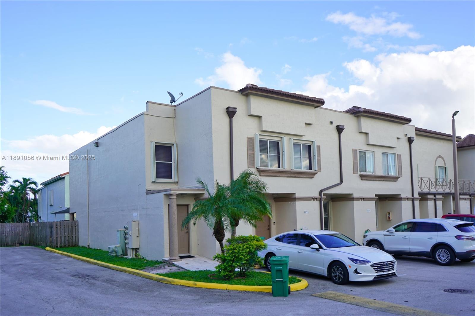 A two-story townhouse exterior features beige stucco walls, a small palm tree, and parked cars — 1195 NW 124th Ave # 2202, Miami FL 33182, MIAMI, FL