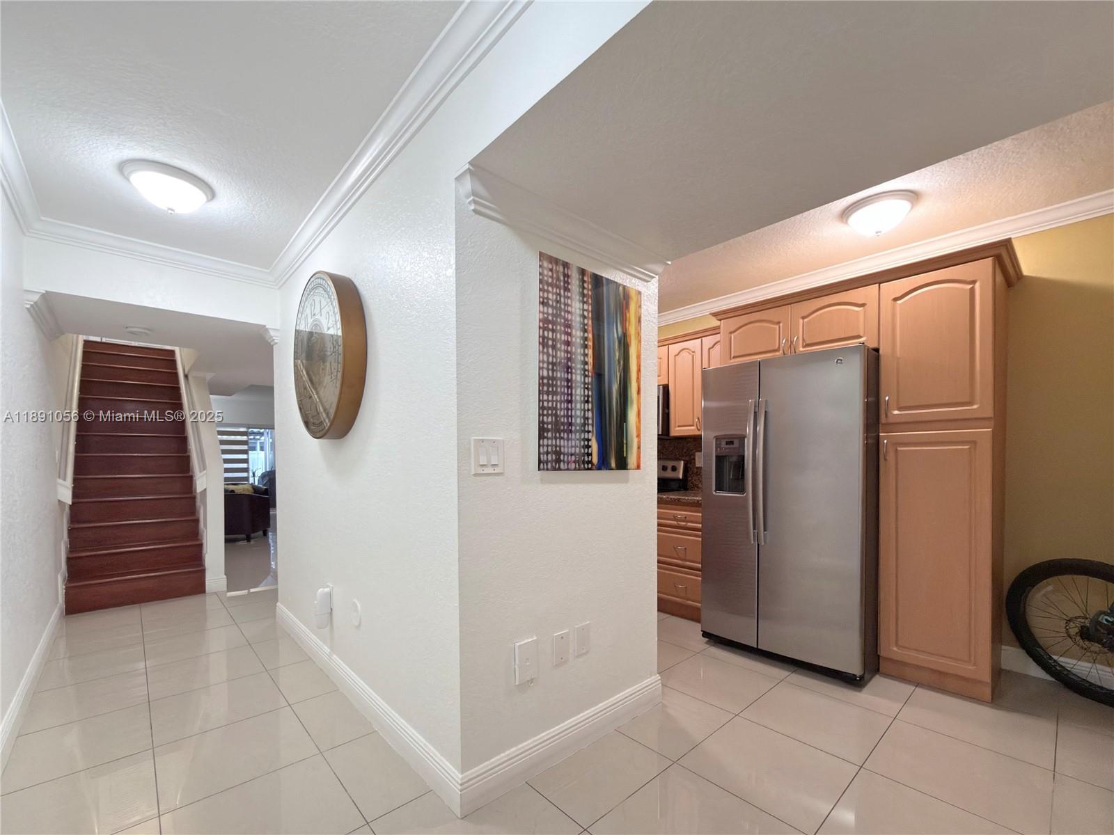 A hallway with a staircase leads to a kitchen featuring light wood cabinets and appliances — 1195 NW 124th Ave # 2202, Miami FL 33182, MIAMI, FL
