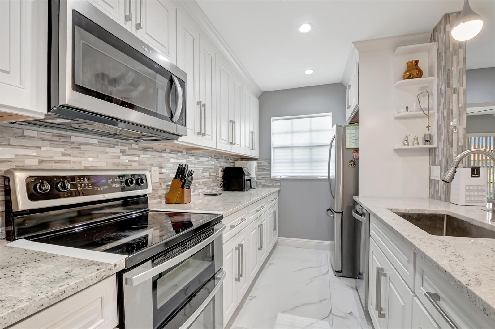 A modern kitchen features white cabinets, stainless steel appliances, granite countertops, and a tiled backsplash — 14010 Nesting Way # B, Delray Beach FL 33484, DELRAY BEACH, FL