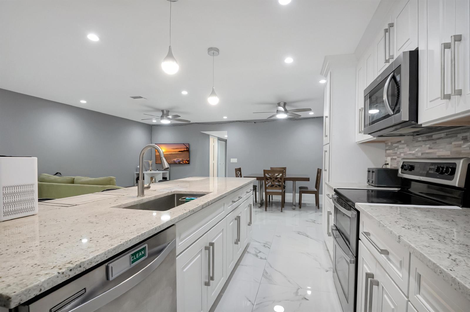 A modern kitchen features white cabinetry, granite countertops, stainless steel appliances, and marble-look tile flooring — 14010 Nesting Way # B, Delray Beach FL 33484, DELRAY BEACH, FL