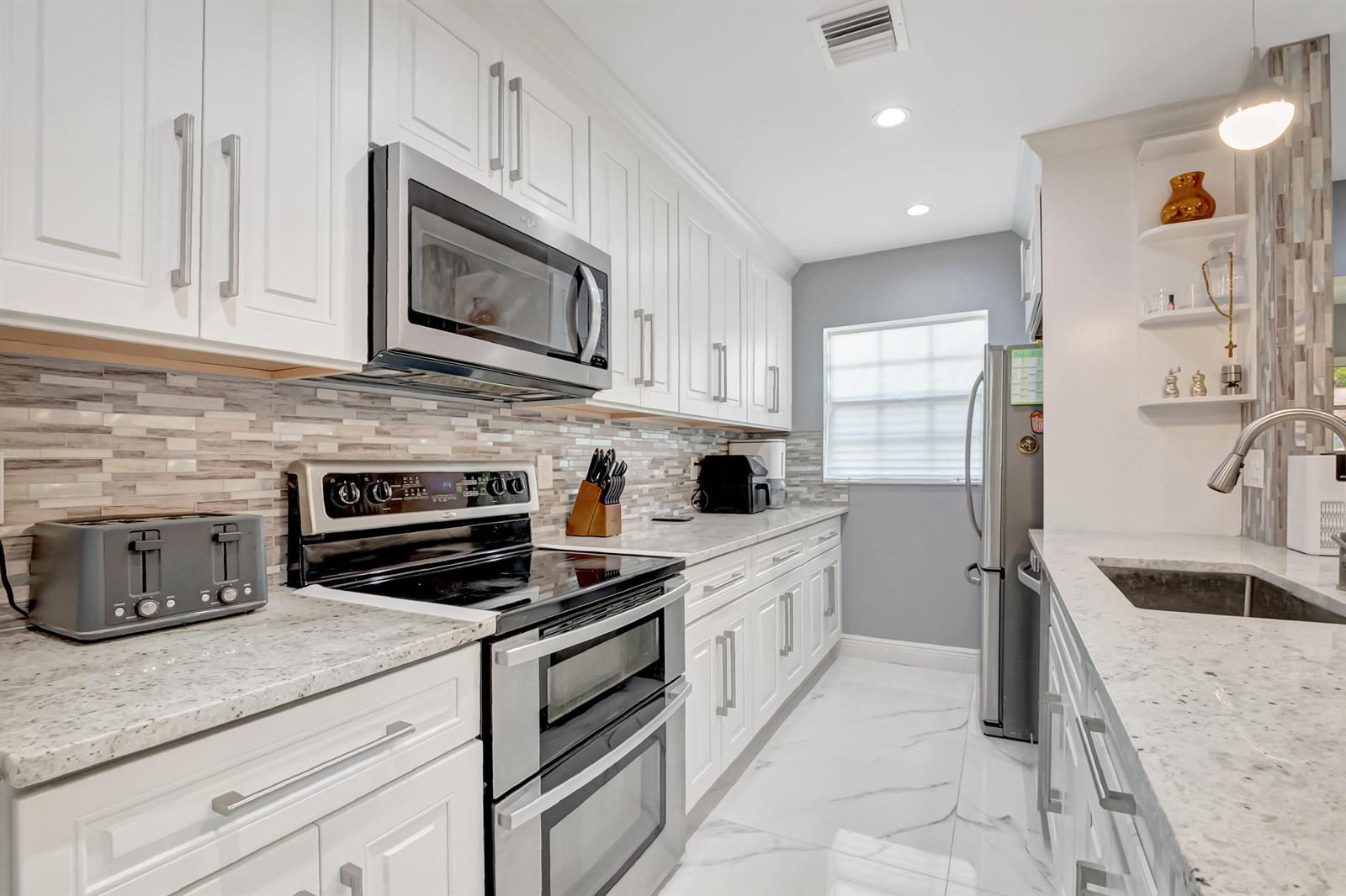 A modern kitchen features white cabinets, stainless steel appliances, and a marble-patterned tile floor — 14010 Nesting Way # B, Delray Beach FL 33484, DELRAY BEACH, FL