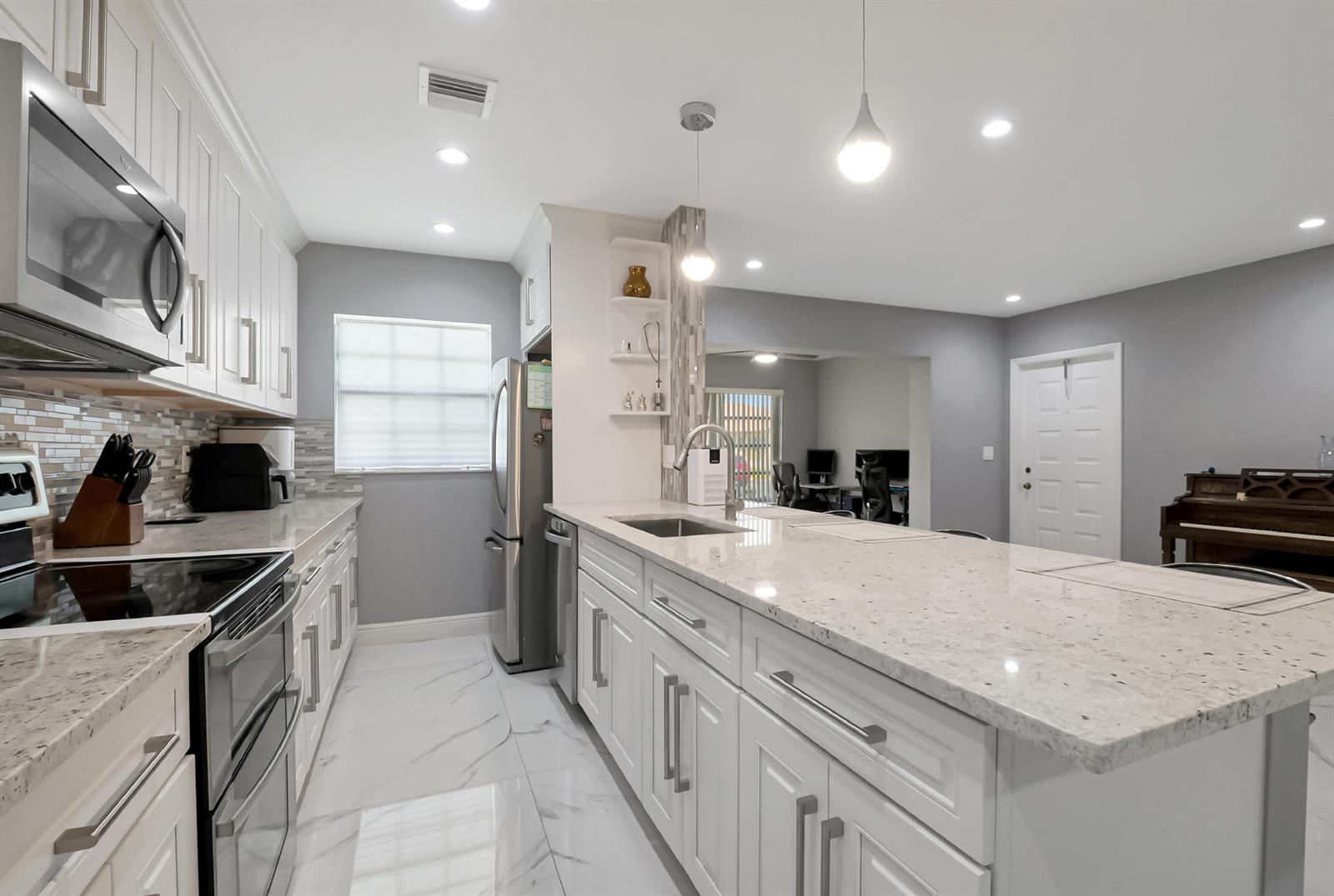 A modern kitchen features white cabinetry, granite countertops, stainless steel appliances, and marble-look tile flooring — 14010 Nesting Way # B, Delray Beach FL 33484, DELRAY BEACH, FL
