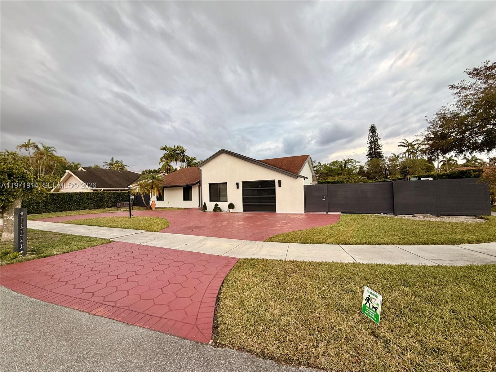 A single-story house features a red patterned driveway, a dark garage door, and a fence — 13253 SW 96th Ter # 0, Miami FL 33186, MIAMI, FL