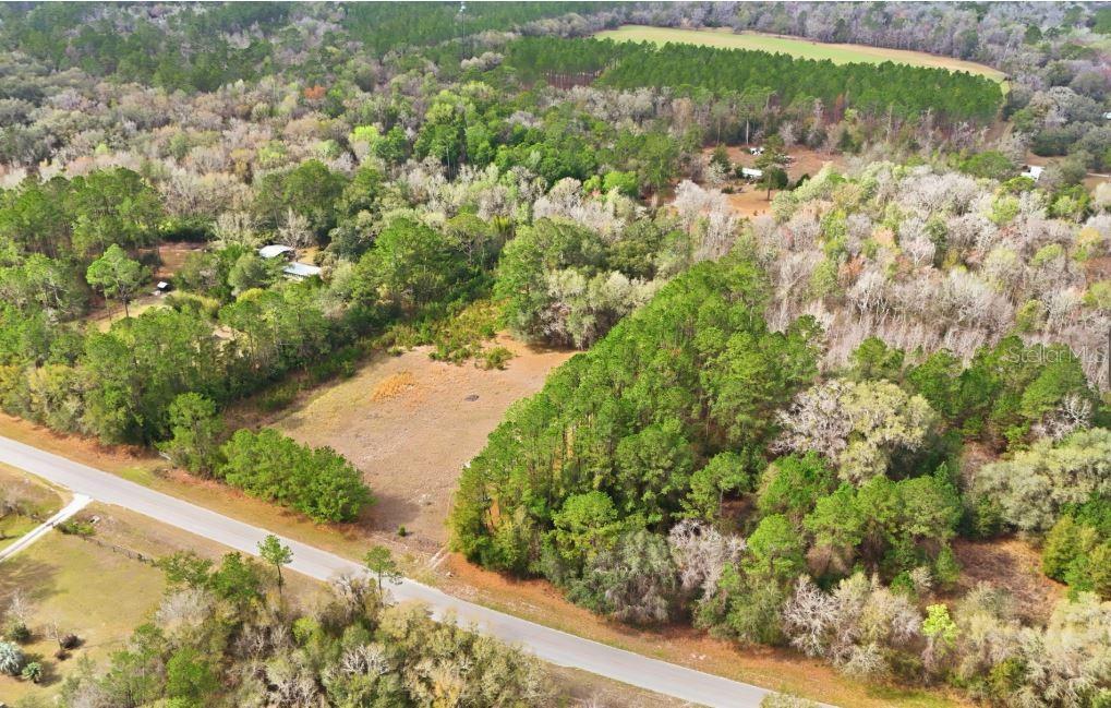 An aerial view shows a cleared, grassy lot bordered by dense trees and a paved road — 17828 NE 21ST STREET, GAINESVILLE, FL