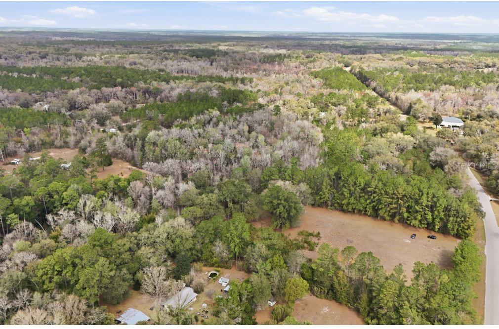 An aerial view shows a mobile home, outbuildings, and scattered debris on a wooded lot — 17828 NE 21ST STREET, GAINESVILLE, FL