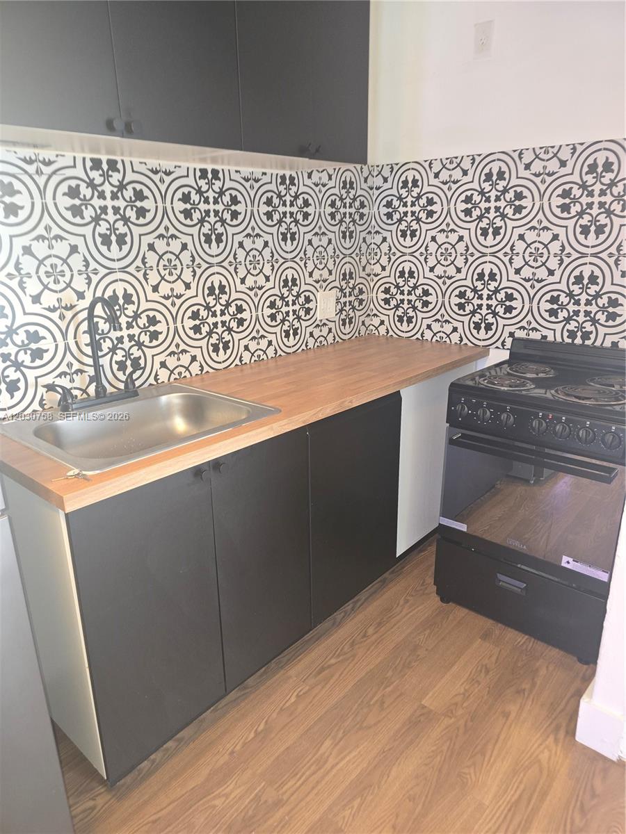 A kitchen features black cabinets, a wood countertop, a stainless sink, and patterned tile backsplash — 66 W 13th St # 3, Hialeah FL 33010, HIALEAH, FL