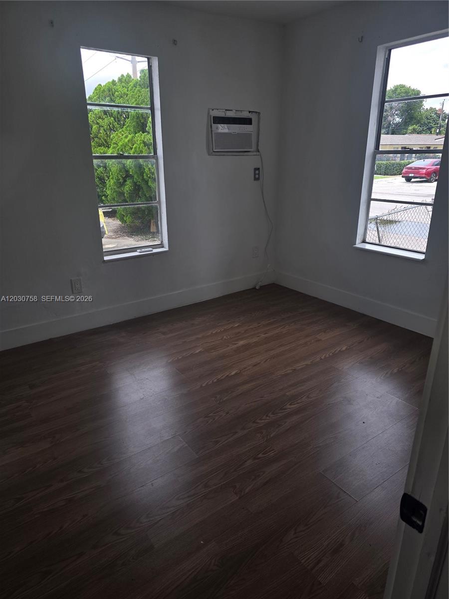 A bedroom with wood-look flooring, two windows, and a wall-mounted air conditioning unit — 66 W 13th St # 3, Hialeah FL 33010, HIALEAH, FL